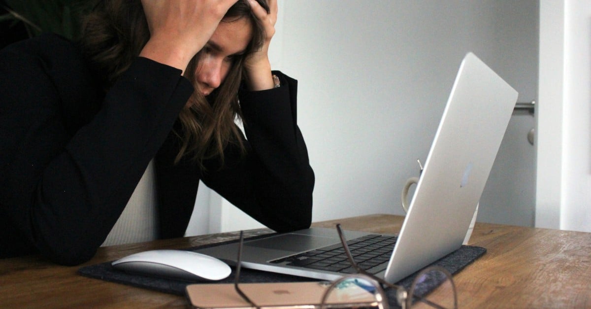 woman holding her face with her hands while looking at a laptop